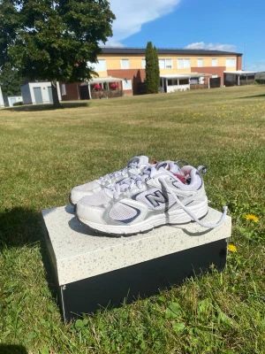 Vita New Balance sneakers - Säljer ett par vita New Balance sneakers med grå och svarta detaljer. Skorna har meshpaneler för extra ventilation och en chunky sula som ger skön komfort. Klassisk New Balance-logga på sidan och vita skosnören. Perfekta för en sportig och trendig look.