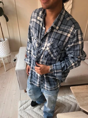 Blå och vit rutig skjorta - Säljer en oversized blå och vit rutig skjorta med långa ärmar och knappar framtill. Skjortan har två bröstfickor med lock och en avslappnad passform. Perfekt för en chill och avslappnad stil.