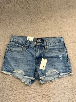 Jeansshorts - Säljer dessa snygga blå jeansshorts från 157 med råa kanter och slitna detaljer framtill. Är i normal/lågmidjad form och har aldrig kommit till användning!