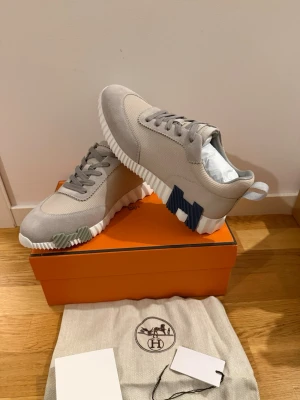 Beige sneakers med kontrastdetaljer - Snygga beige sneakers med ovandel i textil och mocka, samt vita räfflade sulor. Skorna har coola kontrastdetaljer i blått och grönt på sidorna och en dragflik bak. Perfekta för dig som gillar stilrena men unika sneakers.