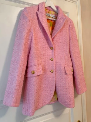 Rosa kavaj från Zara - Stilren rosa kavaj från Zara med guldfärgade knappar framtill och två fickor med lock. Klassisk krage och figurnära passform. Fodret har ett färgglatt mönster som ger en extra twist. Perfekt för dig som vill sticka ut.