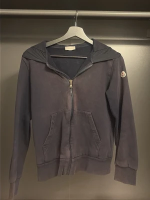 Mörkblå moncler hoodie med dragkedja  - Snygg mörkblå hoodie från Moncler med dragkedja framtill och fickor. Huva med stor Moncler-logga på baksidan och klassisk patch på ärmen. Tillverkad i mjukt bomullsmaterial, perfekt för en avslappnad och trendig look. Kvitto finns