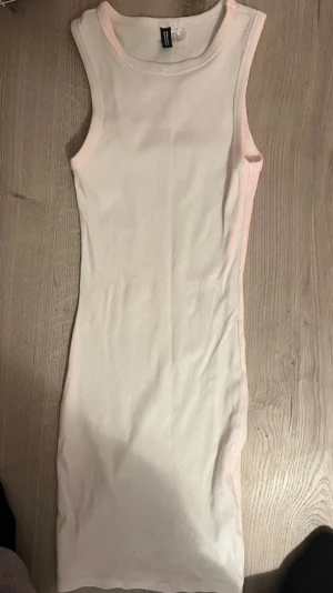 Vit ribbad ärmlös kortklänning - En enkel och stilren vit ribbad klänning i kort modell. Klänningen är ärmlös med rund halsringning och har en kroppsnära passform. Perfekt att styla med sneakers eller sandaler för en fräsch look.