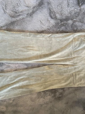 Beige velourbyxor Juicy Couture XS - Säljer ett par beige mjukisbyxor från Juicy Couture i mjuk velour. Byxorna har raka ben och resår i midjan för skön passform. Perfekta för en avslappnad och trendig look. 