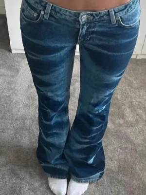Blå bootcut jeans med mönster - Säljer ett par blå bootcut jeans med unikt blekt mönster längs benen. Jeansen har låg midja, klassisk femficksmodell och är tillverkade i denim. Perfekta för dig som vill sticka ut med en retroinspirerad look.