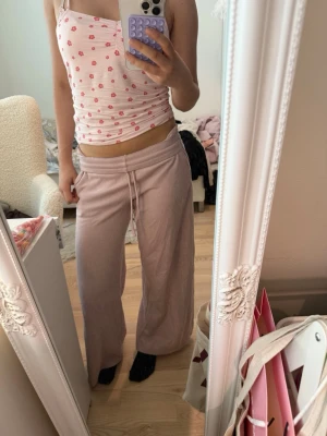 Ljusrosa loungewear-set med linne - Säljer ett ljusrosa loungewear-set med ett ribbat linne med små röda hjärtan och smala axelband samt ett par vida mjukisbyxor med dragsko i midjan. Perfekt för mysiga hemmakvällar och riktigt bekvämt material.