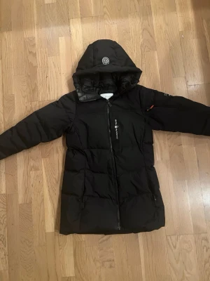 Svart lång dunjacka med huva - Säljer en vinter jacka från sailracing i storlek S . Den är dam men passar lika pts för män , köp gärna ! Bud till 400kr