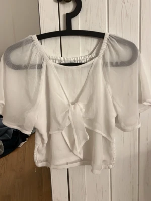 Vit transparent blus med knyt - Säljer en superfin vit blus i transparent material. Toppen har korta ärmar, ett snyggt knyt framtill och en luftig, flowy passform. Perfekt för dig som gillar en lätt och somrig look med trendiga detaljer.