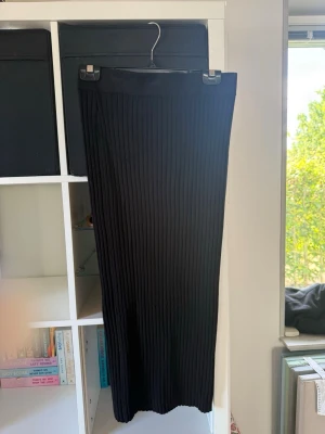 Svart ribbad långkjol från Lindex - Säljer en svart ribbad långkjol i stickat material från Lindex i storlek S. Kjolen har en smal, rak passform. 