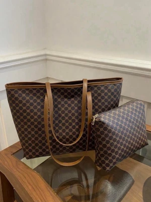 Brun shoppingväska med monogrammönster - Snygg shoppingväska i brunt konstläder med klassiskt monogrammönster och matchande axelremmar. Väskan har en rymlig insida och kommer med en mindre necessär i samma stil. Perfekt för dig som vill ha både stil och funktion i vardagen.