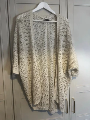 Beige oversize stickad kofta - Säljer en beige, oversize stickad kofta med öppen front och trekvartsärmar. Koftan har ett grovmaskigt mönster och ribbade kanter. Perfekt att slänga över en topp för en avslappnad look.