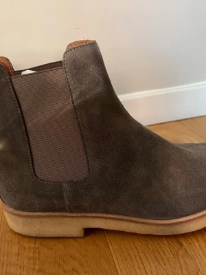 Common Projects- Grå Chelsea boots i mocka - Snygga Chelsea boots i grå mocka med klassisk resår på sidorna och ljus sula. Skorna har en stilren och tidlös design som passar perfekt till jeans eller chinos. Ovandelen är i mjukt mockamaterial och sulan är i gummi för bra komfort.