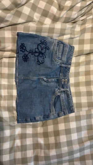 Y2K Floral embroidered mini skirt  - Bought this skirt a while ago and decided to embroider it and then hem it by hand. Selling it bc it doesn’t fit anymore. I’ve only worn it a couple of times although it obviously has a couple of flaws like the hemming at the bottom being very sloppy and the pocket where I’ve embroidered doesn’t work anymore since I accidentally mended it shut. Other than that it’s in great condition. It has two buttons on the front and I think the pockets are very cool it’s a eur kids 170 which is about an XS🦭🦭