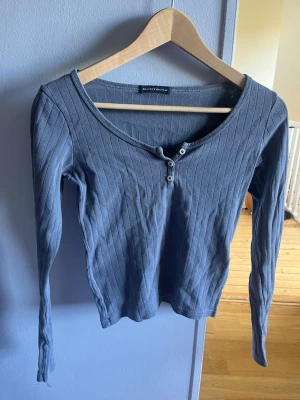Blå ribbad topp från Brandy Melville - Säljer en blå långärmad topp från Brandy Melville. Toppen är ribbad med v-ringning och två knappar framtill. Köpt för ungefär 2-3 år sen, inte använt på ett tag. Någon tråd lös här och där (2-3) men annars är den hel och felfri. Storlek är one size men den passar mig som är xs-s