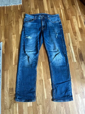 Blå slitna raka jeans - Säljer ett par blå jeans med raka ben och slitningar på låren och knäna. Modellen är thinn finn i strlk 34/32