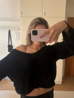 Svart croppad stickad tröja - Säljer en svart, croppad stickad tröja med lös passform och bred halsringning som kan bäras off-shoulder. Tröjan har långa ärmar och är tillverkad i ett mjukt, tunt stickat material. Perfekt för en avslappnad och trendig look.