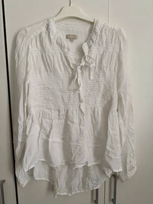 Blusar från Stories - Två blusar från Stories, en vit och rosa. Köpta second hand. Tunna med smockdetaljer över bröstet och ett dekorativt knytband vid halsen. Går att köpa seperat om man är intresserad av en. 