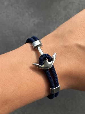 Marint armband med ankardetalj - Snyggt armband med marinblått rep och en silverfärgad ankare som lås. Armbandet har en modern och stilren design med metalliska detaljer som ger en nautisk känsla. Perfekt accessoar för dig som gillar havsinspirerad stil.