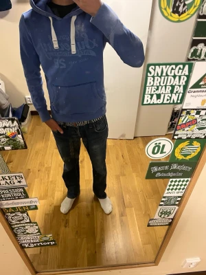 Blå superdry hoodie - Säljer en blå hoodie med vitt tryck framtill och stora vita snören i huvan. Hoodien har en klassisk känguruficka och ribbade muddar vid ärmar och nederkant. Perfekt för en avslappnad och cool stil. Den är S men Superdry sitter tajt som du ser på bilden 