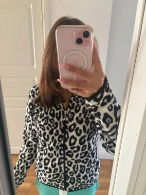 Leopardmönstrad ziptröja - Snygg ziptröja med svartvitt leopardmönster och dragkedja framtill. Tröjan har lång ärm och är gjord i ett mjukt, fluffigt material som känns riktigt cozy. Perfekt för dig som vill sticka ut med ett djurmönster i garderoben.