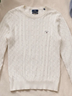 Vit kabelstickad tröja Gant - Snygg kabelstickad tröja från GANT i storlek S. Stilren off-white färg med klassiskt kabelstickat mönster och GANT-logga på bröstet. Perfekt till både vardag och en lite mer uppklädd stil. Fint skick. Priset kan diskuteras vid snabb affär. Bara skriv om mer bilder så fixar ja