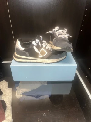 Philipe model sneaker - Snygga svarta sneakers med vita detaljer och reflex på sidan. Skorna har vit sula med svarta inslag och vita skosnören. Ovandelen är i en mix av mocka och textil för en cool look. Perfekta för dig som gillar streetstyle och vill sticka ut. Philipe modell 