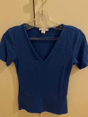 Blå t-shirt med v-ringning Amisu - Snygg blå t-shirt från Amisu med djup v-ringning och korta ärmar. Modellen är figurnära och enkel, perfekt att matcha med jeans eller kjol. Tillverkad i mjukt och stretchigt material för en bekväm känsla.
