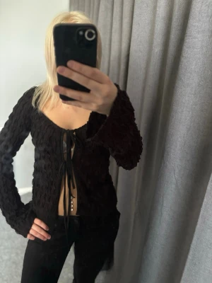 Svart snörad topp från SHEIN - Trendig svart topp från SHEIN med lång ärm och snygg snörning framtill. Toppen har en croppad passform och är gjord i ett våfflat, stretchigt material av polyester och elastan. Perfekt för dig som vill ha en edgy och unik look.