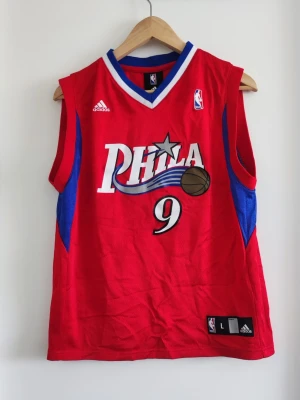Röd Philadelphia 76ers basketlinne - Säljer ett rött basketlinne från Adidas med Philadelphia 76ers tryck och nummer 9, Iguodala på ryggen. Linnet har blå och vita detaljer, ärmlös design och är gjort i ett lätt, ventilerande material perfekt för basket eller träning.