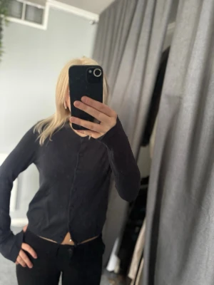 Svart kofta från 157, storlek S - Svart, tunn och figurnära kofta från 157 med långa ärmar och knäppning framtill. Klassisk ribbad kant vid halsringning och ärmslut. Perfekt att styla med jeans eller kjol för en clean look.