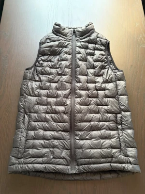 Grå dunväst från Everest - Snygg grå dunväst från Everest med quiltad design och hög krage. Västen har dragkedja framtill och två sidofickor. Perfekt för lager-på-lager och håller dig varm under kyliga dagar. Enkel och stilren look som passar till det mesta.