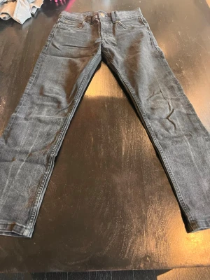 Grå slim fit jeans från Lee - Snygga grå slim fit jeans från Lee med klassisk femficksdesign och knappgylf. Jeansen har en tvättad look och smal passform som sitter tajt längs benen. Perfekta för dig som gillar en stilren och enkel vardagsstil.