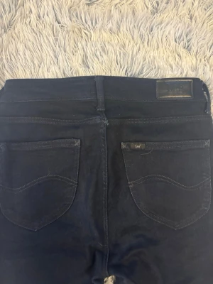 Mörkblå Lee jeans med raka ben - Snygga mörkblå jeans från Lee med klassiska fem fickor och raka ben. Jeansen har Lee-logga på bakfickan och läderpatch i midjan. Tillverkade i slitstark denim med snygga sömdetaljer. Perfekta för en avslappnad och trendig look.
