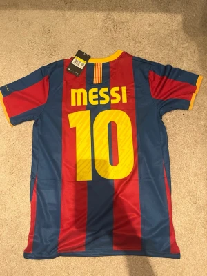 Barcelona Messi matchtröja Nike - Säljer en officiell FC Barcelona matchtröja från Nike med Messi och nummer 10 på ryggen. Tröjan har blå och röda vertikala ränder, gula detaljer vid krage och ärmslut samt klubbmärke och Unicef-logga på bröstet. Tillverkad i lätt och ventilerande Dri-FIT-material.