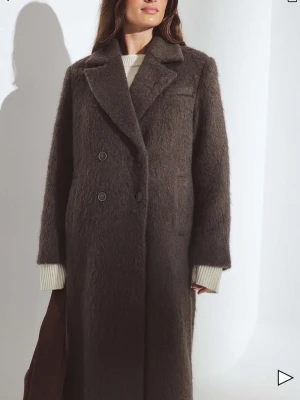 Brun lång dubbelknäppt kappa - Helt oanvänd kappa från NA-KD. Säljer eftersom den inte är helt min stil. Kammad ullblandning, storlek 34. Nypris 1099 kr.