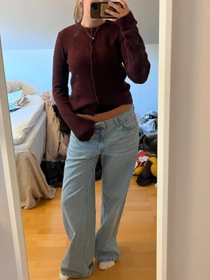 Vinröd stickad cardigan med knappar - Mysig vinröd stickad cardigan med långa ärmar och knäppning framtill. Tröjan har en enkel, klassisk design och är lätt att matcha med olika outfits. Perfekt för dig som gillar en avslappnad men ändå stilren look.