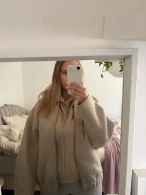 Beige teddyjacka med dragkedja - Mysig beige teddyjacka med dragkedja framtill och avslappnad passform. Jackan har långa ärmar och resår vid nederkanten för en skön och trendig look. Perfekt för kyliga dagar när du vill vara både varm och stylish.