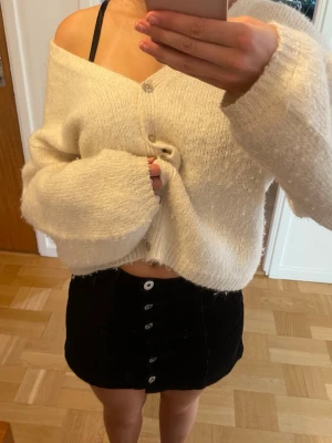 Svart manchesterkjol med knappar - En svart kort manchesterkjol med raka linjer och knappar framtill. 