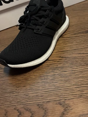 Svart vitta  Adidas ultra boost - Svarta sneakers från Adidas med stickad ovandel och klassiska tre ränder på sidan. Skon har en vit, dämpad sula och svarta snören. Perfekt för dig som gillar att träna eller springa men även vara ta de lugnt på dagarna.