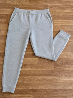 Polo Ralph Lauren grå mjukisbyxor 🐎 - Klassiska ljusgrå mjukisbyxor från Polo Ralph Lauren med mörkblå broderad logga. Dragsko i midjan, sidofickor och muddar vid bensluten. Väldigt stilrena och enkla att matcha. Storlek: Xl barn men passar ca S i vuxenstorlek! Skick: Fint skick men den har några skador! Skriv gärna vid frågor eller om du vill ha mått!