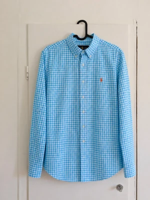 Polo Ralph Lauren rutig skjorta 💙 - Klassisk blå/vit rutig skjorta från Polo Ralph Lauren med broderad orange pony-logga på bröstet. Button-down krage och en tidlös modell som passar perfekt till både vardag, skola, fest eller en clean/preppy outfit. 📏 Storlek: L (14-16) ✨ Skick: Mycket bra men den är lite missfärgad i kragen/nacken! 💙 Färg: Ljusblå/vit 🐎 Broderad Ralph Lauren-logga Säljer då den inte kommer till användning. Hör gärna av dig vid frågor eller om du vill ha fler bilder/mått! 📦
