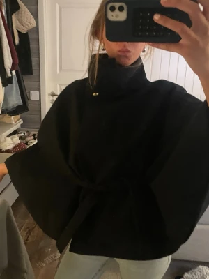 Poncho - Säljer en mörkblå cape-rock med hög krage och knytband i midjan. Rocken har vida ärmar och stängs med knapp upptill. Perfekt för dig som vill ha en stilren och trendig look. Passar till jeans eller kjol för en cool vibe. Från gina young, storlek 164 eller 179 (finns ingen lapp så osäker på storlek) men passar xs/s
