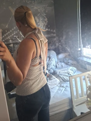 Vit prickig halterneck topp - Säljer en söt vit halterneck topp med svarta prickar och knyt i nacken. Toppen är ärmlös och har en figurnära passform, perfekt för varma dagar. Materialet känns mjukt och lätt mot huden.