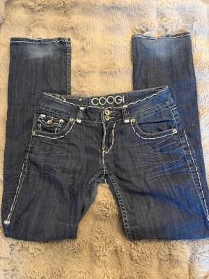 Bootcut jeans med vita stygn och detaljerade bakfickor - Lågmidjade bootcut jeans med tjocka vita stygn och detaljerade bakfickor. Ingen storlek står men uppskattade W28. Slitage finns längst ned på byxorna och en knapp saknas på ena bakfickan men annars i strålande skick. Skriv om du har frågor!💕🙏🏻