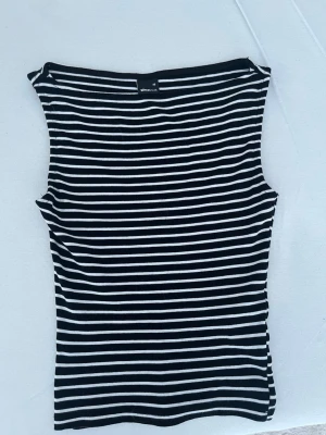 Svartvit randig ärmlös topp - Säljer en svartvit randig ärmlös topp med tight passform. Perfekt till jeans eller kjol för en enkel och stilren look. Tunn och mjuk i materialet, passar bra till varmare dagar.