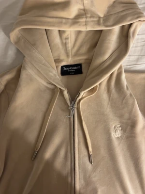 Juicy couture beige set - Säljer en beige velour hoodie från Juicy Couture i storlek XXS. Hoodien har dragkedja, huva med snören och ett broderat JC-logotyp på bröstet. Klassisk juicy-zip med metalländar på snörena och en snygg J-dragkedja. Perfekt för en chill och trendig look. 1300kr för hela setet.