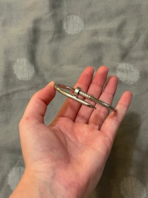 Silvrigt armband i spikdesign - Coolt armband i blankt silverfärgat metallmaterial, format som en böjd spik som snurrar runt handleden. Ger en edgy och modern vibe, perfekt för dig som gillar unika accessoarer och statement-smycken.