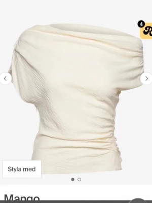 Krämvit asymmetrisk topp från Mango  - Säljer en krämvit asymmetrisk topp från mango med draperad halsringning. Den har en dragkedja på sidan som gör det lättare att sätta på och ta av sig den. Endast använd ett fåtal gånger.