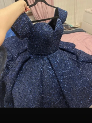 Marinblå glittrig balklänning - Säljer en marinblå långklänning med massor av glitter och en voluminös kjol. Klänningen har en markerad midja, offshoulder-ärmar och en elegant, strukturerad överdel. Perfekt för bal eller andra speciella tillfällen.