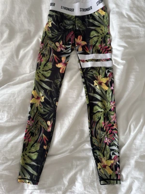 Blommiga tights från Stronger  - Snygga träningstights från Stronger i storlek XS med tropiskt blommönster. Tillverkade i 85% polyester och 15% elastan för skön stretch. Supersköna att träna i eller bara vara hemma.☺️Helt oanvända och köpta på strongens hemsida🩵